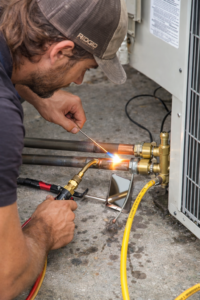 HVAC technician brazing copper refrigerant lines during installation